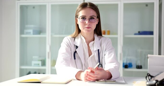 Doctor waving smiling looking at camera and sitting at table in clinic