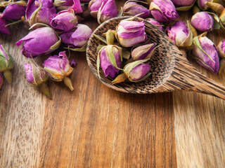 Pink dried rosebuds on a wooden table with a wooden spoon. Close-up. Free space below. Horizontal....