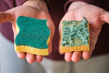 Mens hands comparing new and old double-side cleaning scouring sponge.