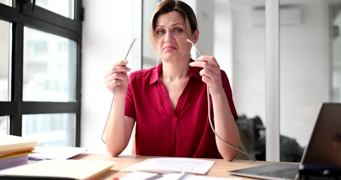 Woman looks with surprise at broken wire in hand in office