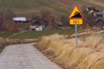 Znak ostrzegawczy o nachyleniu drogi 12% na wiejskiej drodze. 