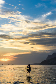 A Man Crouching On A Slackline At Arpoador Beach During The Sunset, Rio De Janeiro, Brazil