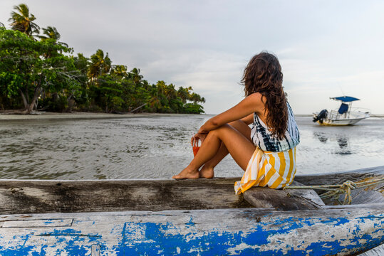 Young woman sitting in canoe by tropical beach, Boipeba Island, South Bahia, Brazil