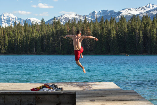 Man in swimming trunks jumping into Annette Lake from jetty, Jasper National Park, Alberta, Canada