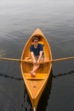 A young man rows a small antique wooden row boat on the St. Lawrence River in upstate New York's 1000 Islands.