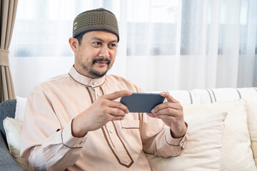 Happy young Asian Muslim man using a mobile phone at home
