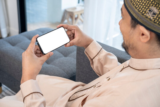 Happy young Asian Muslim man using a mobile phone at home