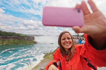 A female tourist takes a selfie with  Niagara Falls in the background.