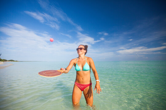 A young woman plays racquetball on the beach.