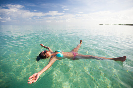 A young woman floats on her back in shallow turquoise water.