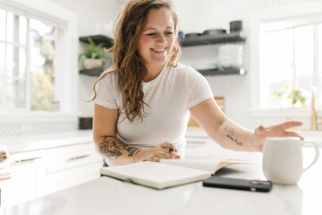 Smiling grown woman journaling and reaching for white mug of coffee