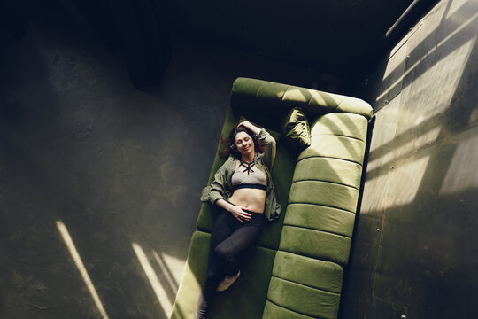 Smiling woman on the couch, listening to cheerful music in headphones.