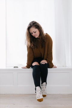 Cozy grown white woman in knit sweater and smiley socks in window seat