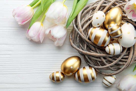 Nest with Easter eggs painted golden colors on a white wooden background.