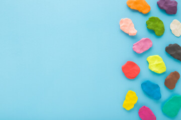 Kneaded multicolor modeling clay on light blue table background. Pastel color. Closeup. Preparing material for making different colorful shapes. Empty place for text. Top down view.