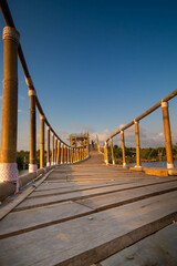 Obraz premium A wooden bridge built at the mouth of a river where there is a mangrove forest while sunset.