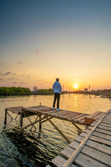 Fototapeta premium Someone standing at a wooden bridge built at the mouth of a river where there is a mangrove forest while sunset.
