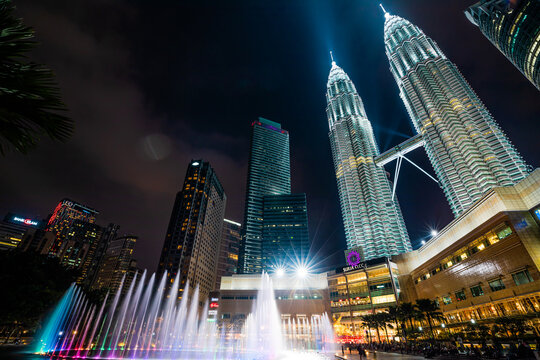 Kuala Lumpur, Malaysia - January 2023: The Petronas Twin Towers are lit up at night in the Suria Mall area, accompanied by beautiful fountains and a nightlight show.