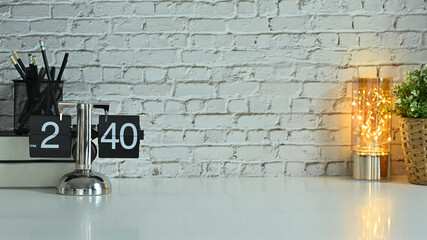 A vintage flip clock, pencil holder, books and houseplant on white table against brick wall. Copy space for your text