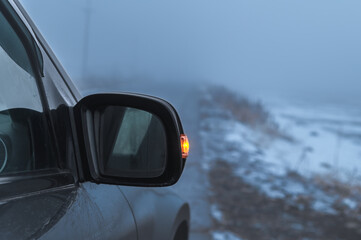 Mirror of a car on a rural road on a foggy winter day. A small light in the fog.