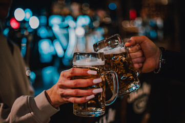 man and woman hands toasting with glasses of light beer at the pub or bar