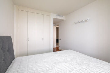 Modern bright bedroom with a bed and built-in wardrobe and an open door to the corridor. Minimalistic but cozy design concept. Hotel or rental apartment design