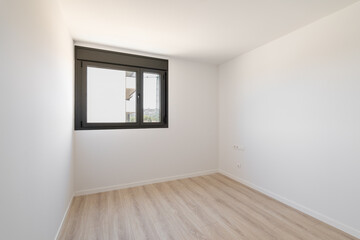 Small empty room without furniture. The floor is new light wood laminate. A window made of black plastic for airing the room. Daylight enters through the frosted glass in the window.