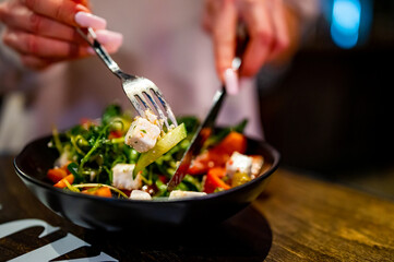 Woman's hands eat salad on table in restaurant