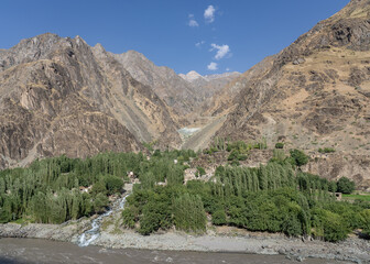 Landscape view of mountain village amidst trees and torrent on Afghan side of Panj river valley, seen from Darvaz district, Gorno-Badakshan, Tajikistan Pamir