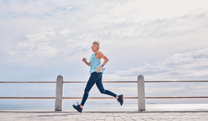 Senior woman running outdoor at on sky mockup at beach promenade for energy, health and cardio workout. Elderly female, exercise and runner at ocean for sports training, fitness and healthy marathon