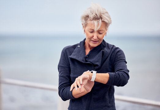 Smart watch, senior woman and fitness outdoor at beach promenade, exercise or sky mockup. Stopwatch, sports lady and runner check time, heart rate and monitor healthy body progress, clock or data app