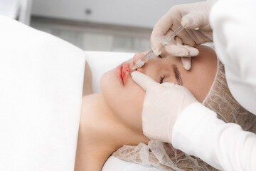 Obraz na płótnie Canvas close-up, female lips. Surgeon, in medical gloves, carefully and slowly injects hyaluronic acid into woman's lips with a syringe. lip augmentation procedure. beauty injections. Plastic surgery.