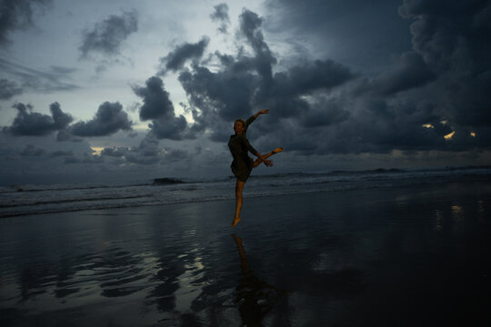 Silhouette of happy joyful woman jumping and having fun at the beach against the sunset.