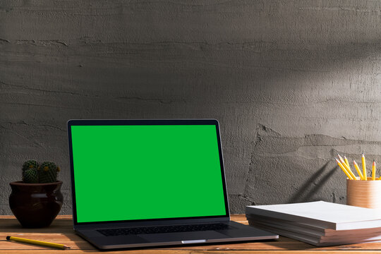 Chroma key green screen, angled view laptop on table with blank cover magazine stack