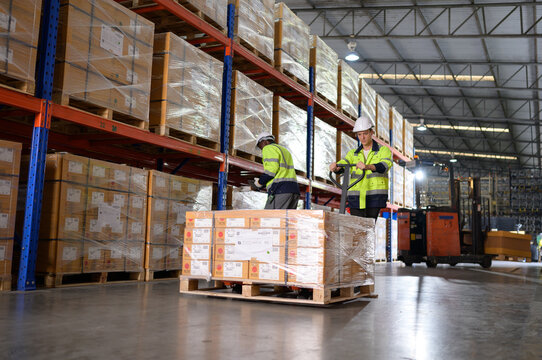 Worker in auto parts warehouse use a handcart to work to bring the box of auto parts into the storage shelf of the warehouse waiting for delivery to the car assembly line