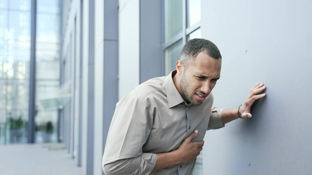 A man experiences a sharp pain in his chest standing on the street near an office building. A sick male of mixed race suffers from tension in the chest. He feels bad, has a heart attack. He needs medi