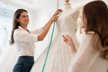 Caucasian female fashion designer being helped her customer choose wedding dress in the salon