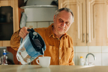 elderly man pours water into a cup from the filter in the kitchen