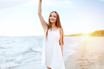 Fototapeta na wymiar Happy smiling woman in free happiness bliss on ocean beach catching clouds. Portrait of a multicultural female model in white summer dress enjoying nature during travel holidays vacation outdoors