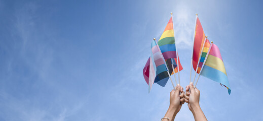 LGBTQ+ flags holding in hand, cloudy and bluesky background, copy space, concept for LGBTQ+ people community celebrations in pride month, June, around the world.