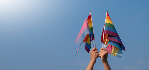 LGBTQ+ flags holding in hand, cloudy and bluesky background, copy space, concept for LGBTQ+ people community celebrations in pride month, June, around the world.