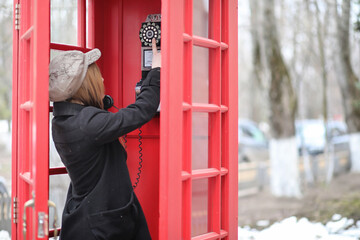 Beautiful young girl in a phone booth. The girl is talking on the phone from the payphone. English...