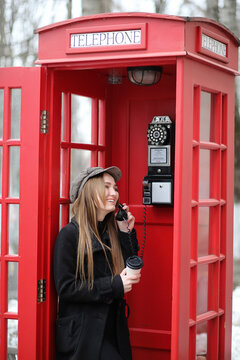 Beautiful young girl in a phone booth. The girl is talking on the phone from the payphone. English telephone booth in the street and a woman talking on phone.