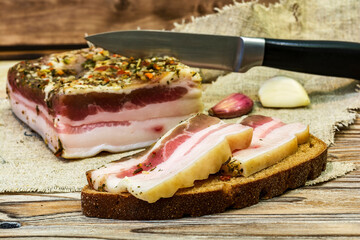 Two slices of salted bacon on black bread lie on the table