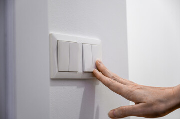 Close-up of a woman's finger turns on or off a light switch with a white wall at home. Power, energy, electricity saving.