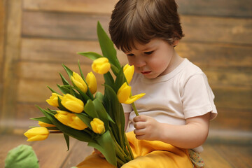 A small child with a bouquet of yellow tulips. A boy with a gift of flowers in a vase. A gift for girls on a female holiday with yellow tulips on the floor.