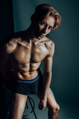 Fototapeta na wymiar hot male model sit nude and erotic in dark blue studio on stool express his masculine body shaped by fitness and aesthetics as symbol for traditional gender expression while being macho and sex symbol