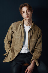 edited and retouched portrait of young man and student in an artificial way sit on barstool with green jacket and hand in pocket