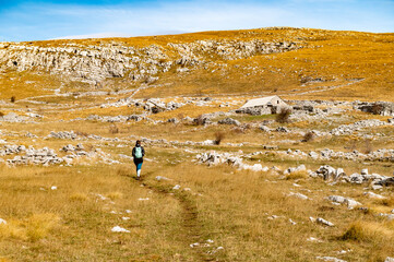 Autumn Dinara mountain landscape with sporty young woman, rocky hills, golden grass, sky. Travel and tourism. Hiking female in Dinaric Alps on the border between Croatia and Bosnia and Herzegovina.