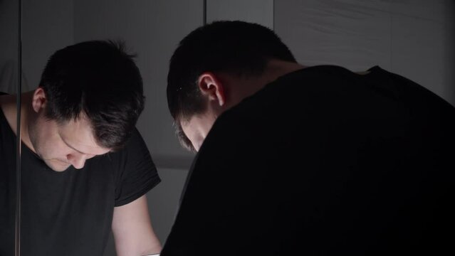 Young angry man breathing deeply and looking in his reflection in mirror. Concept of depression, suicide, stress, mental illness, loneliness and frustration